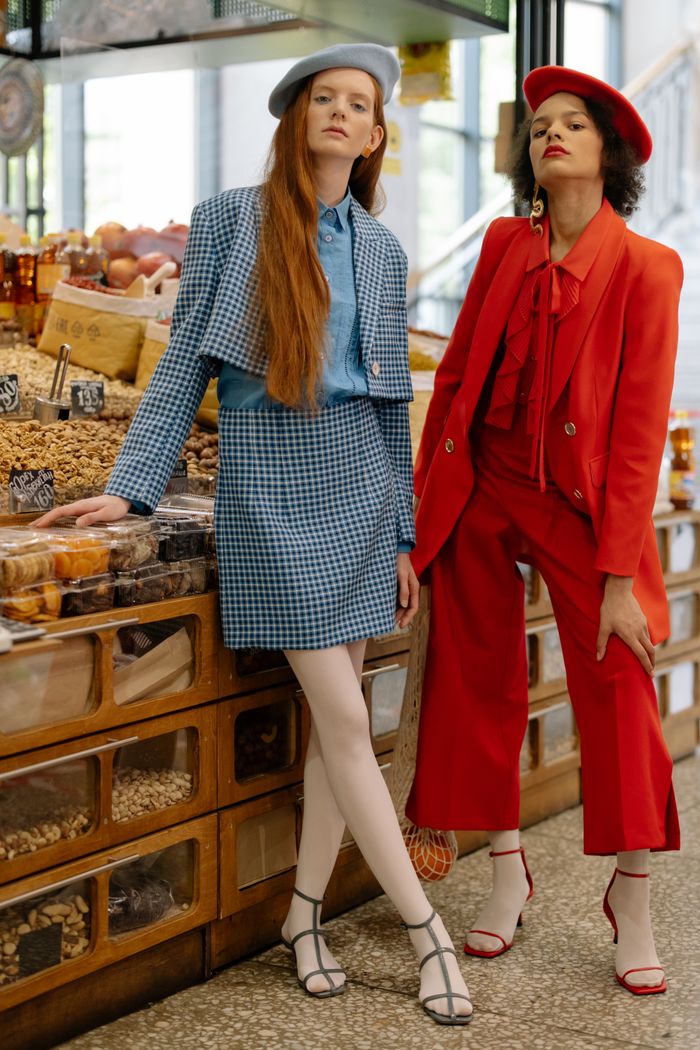 Two fashionable women pose confidently in vibrant outfits at a market.
